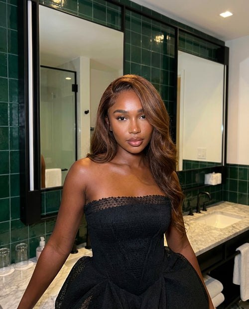 Woman in a black dress standing in a bathroom with green tiles.