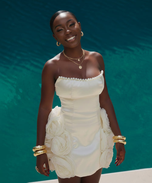 Woman in a white strapless Olivia dress by Nalowa with floral details against a teal background